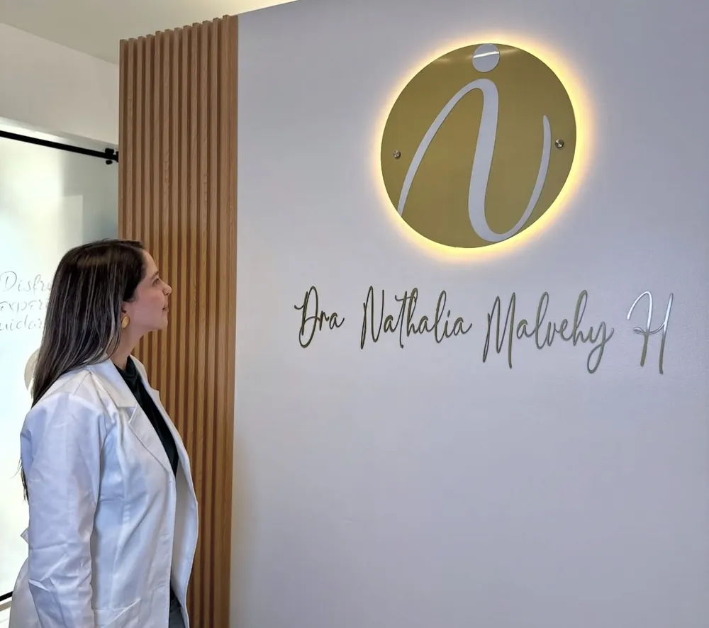 La Dra. Nathalia Malvehy mirando el logo iluminado de su consultorio